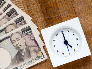 Time is money, clock and Japanese 10000 yen bills on the wooden