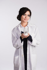 Beautiful young brunette female nurse or physician with glasses in blue dress and white lab coat holding a bottle of pills