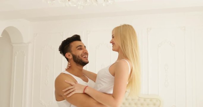 Young happy couple embrace woman run and jump over man hug spin around modern home bedroom circling
