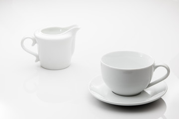 Cup and saucer set with matching creamer container on a white ba