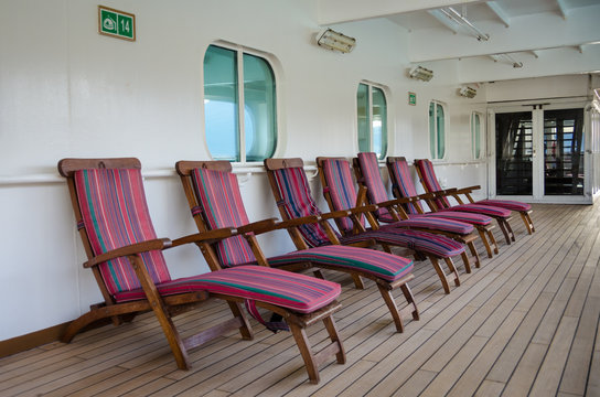 Colorful wooden deck chairs are set out for passengers on the promenade deck of a cruise ship.