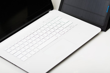 Nice black portable solar charger sitting next to exclusive white laptop, modern business technology concept, studio background