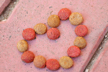 Closeup fresh red and brown colored crunchy dog food lying on stone tiles surface, shaped in heart formation