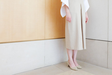 woman standing in corner beige dress with mid heel shoe minimal style. - obrazy, fototapety, plakaty