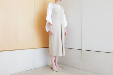 woman standing in corner beige dress with mid heel shoe minimal style. 