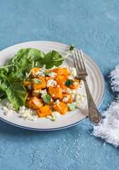 Baked pumpkin and goat cheese salad on a blue background. Healthy food