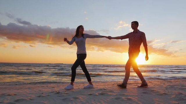 Steadicam shot: Loving couple walking at sunset on the beach or lake. She leads the guy flirting
