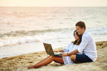 Beautiful romantic couple relaxing on the beach . By browsing on the laptop