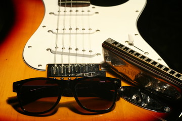 Vintage electric guitar, harmonica, sunglasses on black background