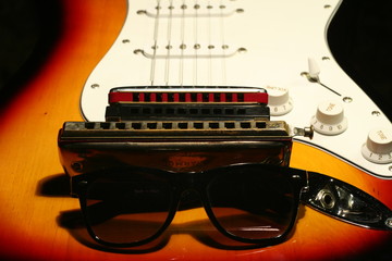 Vintage electric guitar, harmonica, sunglasses on black background