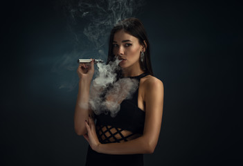 Sexy girl in a black dress smoking electronic cigarette