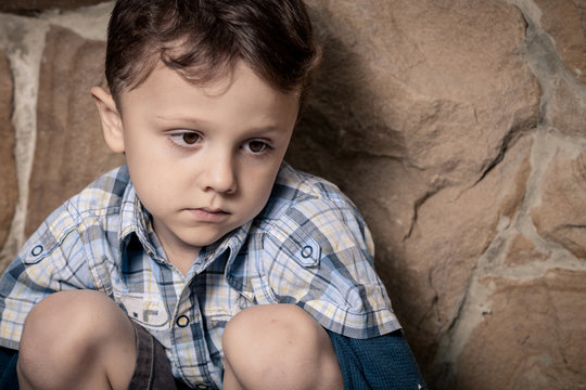 sad little boy sitting near the wall
