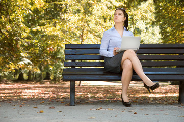 Obraz premium Sexy young businessgirl works with her laptop on the bench in the park