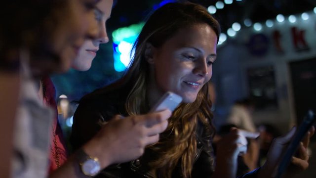 Female friends laugh together as they share things on their phones and tablet