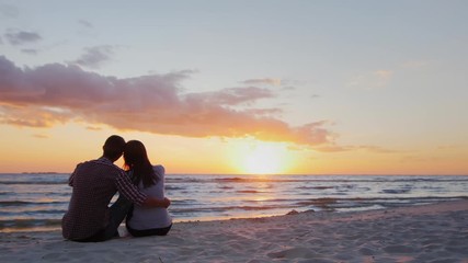 A young couple admiring the sunset at sea. Sit in an embrace on the sand