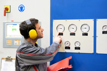 Industriearbeiter mit Gehörschutz in einer Anlage ließt Messwerte einer Maschine ab // Industrial...