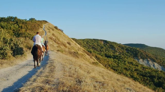Group of people ride horses by gorgeous mountainside trail. Family on horseback riding trip on mountain trail