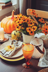 autumn traditional seasonal table setting at home with pumpkins, candles and flowers, selective focus