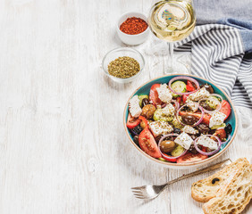 Greek salad with bread, oregano, pepper and glass of white wine over old white painted wooden board, top view, selective focus, copy space