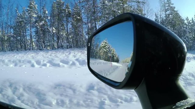 Winter road in the countryside. Forest, blue sky and sunlight. Rear view mirror