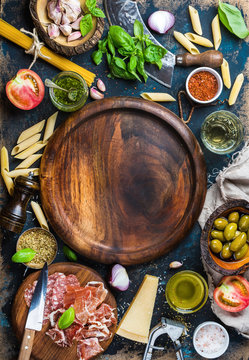 Italian food cooking ingredients on dark plywood background with round wooden tray in center, top view, copy space, vertical composition