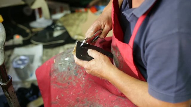 Calzolaio al Lavoro nella sua bottega artigianale. Foratura a pinza per chiodi. 