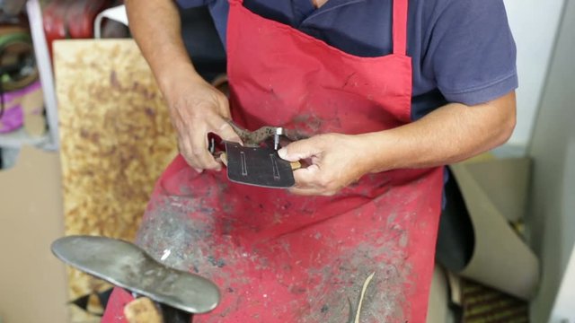 Calzolaio al Lavoro nella sua bottega artigianale. Foratura a pinza per chiodi. 