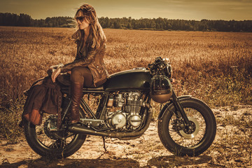 Stylish woman on the vintage custom cafe racer in a field.