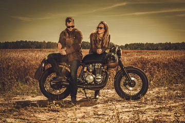 Fototapeta na wymiar Stylish cafe racer couple on the vintage custom motorcycles in a field.