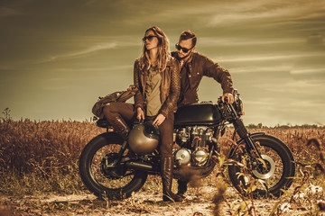 Obraz na płótnie Canvas Stylish cafe racer couple on the vintage custom motorcycles in a field.