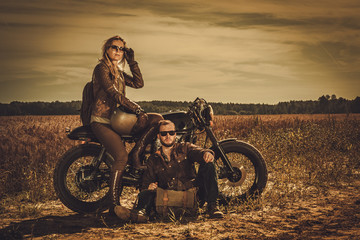 Plakat Stylish cafe racer couple on the vintage custom motorcycles in a field.