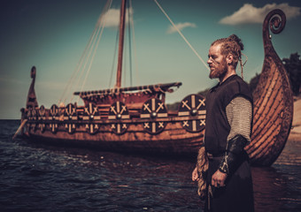 Viking warrior with sword standing near Drakkar on the seashore.