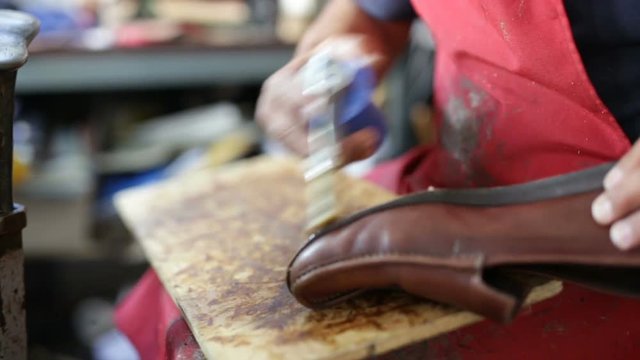 Calzolaio al Lavoro nella sua bottega artigianale. Incollatura suola mocassino marrone uomo. 