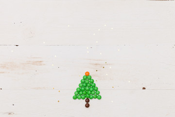 Top view on a small funny Christmas tree made of candies with golden stars confetti on white wooden background. Christmas and Happy New Year concept