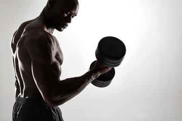 Muscular young bodybuilder exercising with dumbbells