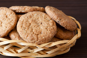 Pile of chocolate chip cookies in the wicker bowl on dark background. Close-up, selective focus.