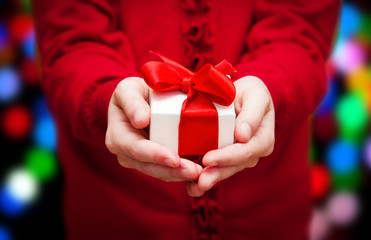 Person in red holding Christmas gift box with Christmas lights behind