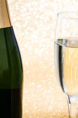 Glass cup with champagne bottle on golden brilliant background

