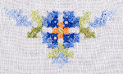 Blue flower triangle motiv hand embroidery on white linen tablecloth.  Multicolored cross stich decoration with yarn. Handicraft. Macro photo close up from above.