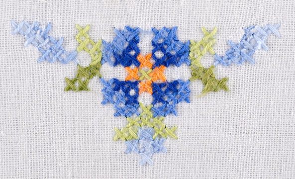 Blue flower triangle motiv hand embroidery on white linen tablecloth.  Multicolored cross stich decoration with yarn. Handicraft. Macro photo close up from above.