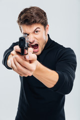 Fototapeta na wymiar Angry irritated young man aiming gun on you and shouting