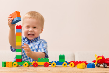 Portrait of child playing with colorful plastic bricks at the table. Toddler having fun and building a train out of constructor bricks. Early learning. Developing toys