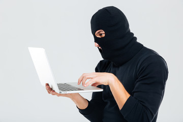 Portrait of man in balaclava standing and using laptop