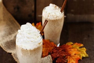 Pumpkin Spice Iced Coffee with whipped cream and cinnamon against a rustic background. Shallow depth of field with selective focus on Latte in foreground.