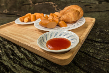 Sausage and Croissant baked on wooden plate with copy space.