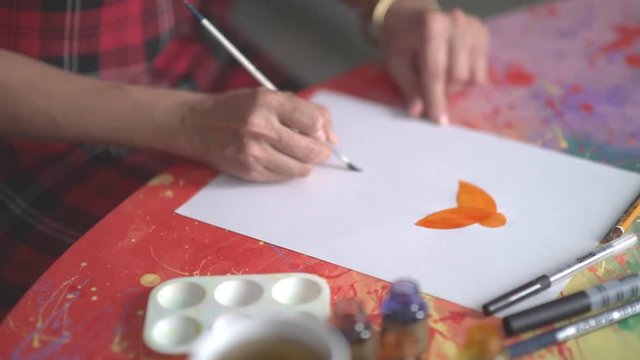 The artist draws a brush. Hands of the artist with a brush. The artist paints a woman's silhouette. Orange watercolor paint. Drawing watercolor. Drawing lessons