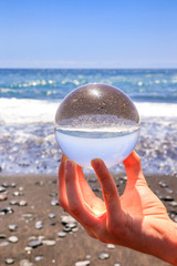 Hand holding glass sphere at beach and sea