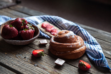 delicious breakfast with strawberries and sweet bun on wooden background. Fruit, food, chocolate