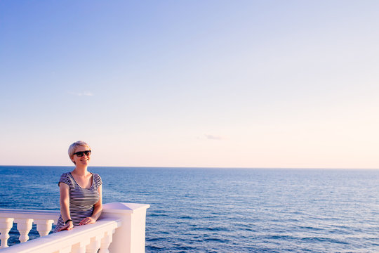 cute blondy woman on balcony looking at the ocean. travel concept