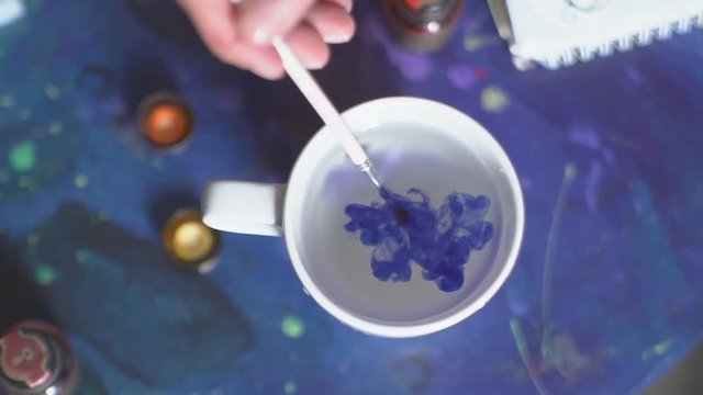 The white glass with clear water dunk a brush with blue paint. Water glass is colored in blue.